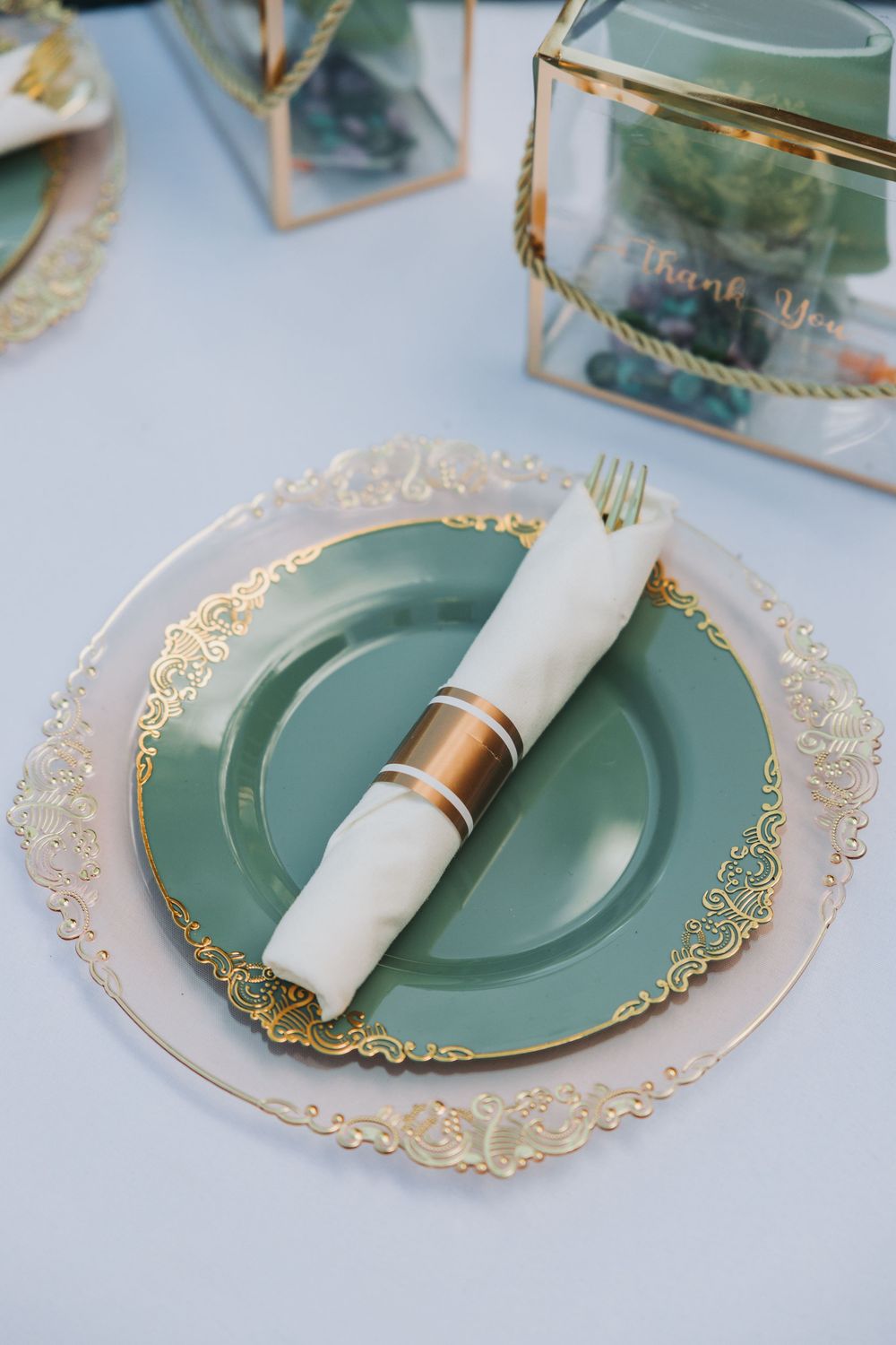 Elegant place setting with mint green and gold-rimmed plates, white napkin, and copper napkin ring on white tablecloth.