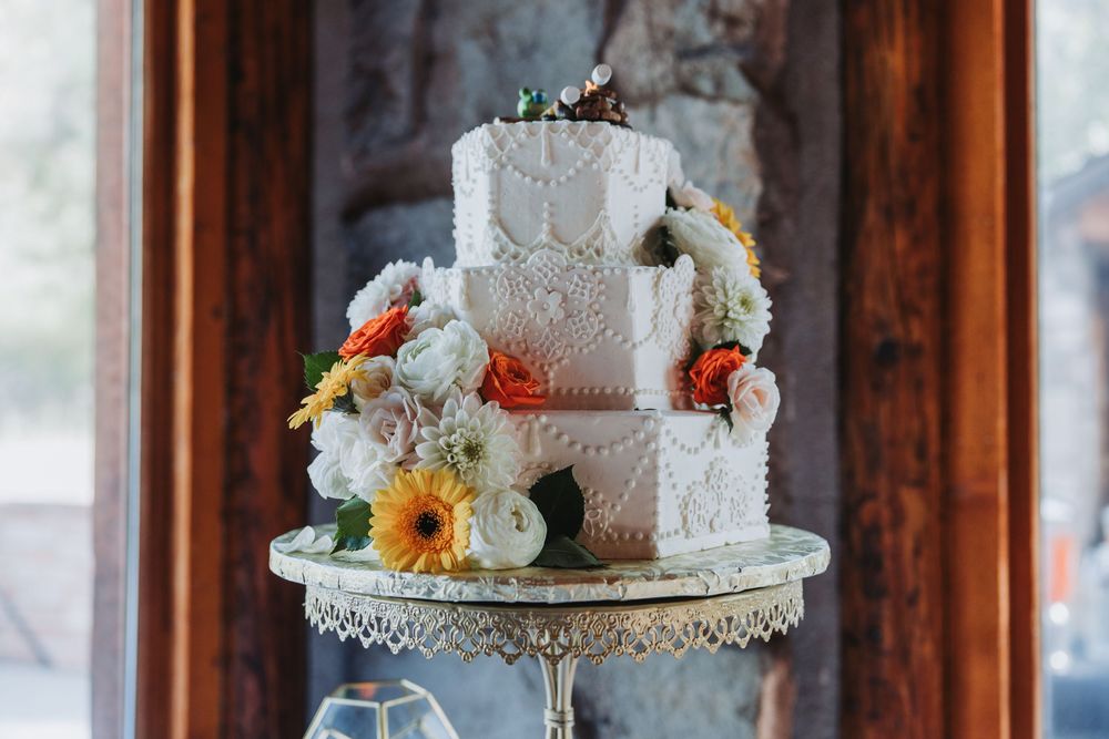 Elegant white wedding cakes decorated with fresh flowers and lace details displayed on rustic wooden tables.