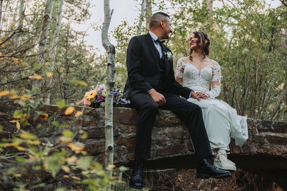 A couple shares a romantic moment in a wooded outdoor setting during their wedding celebration.