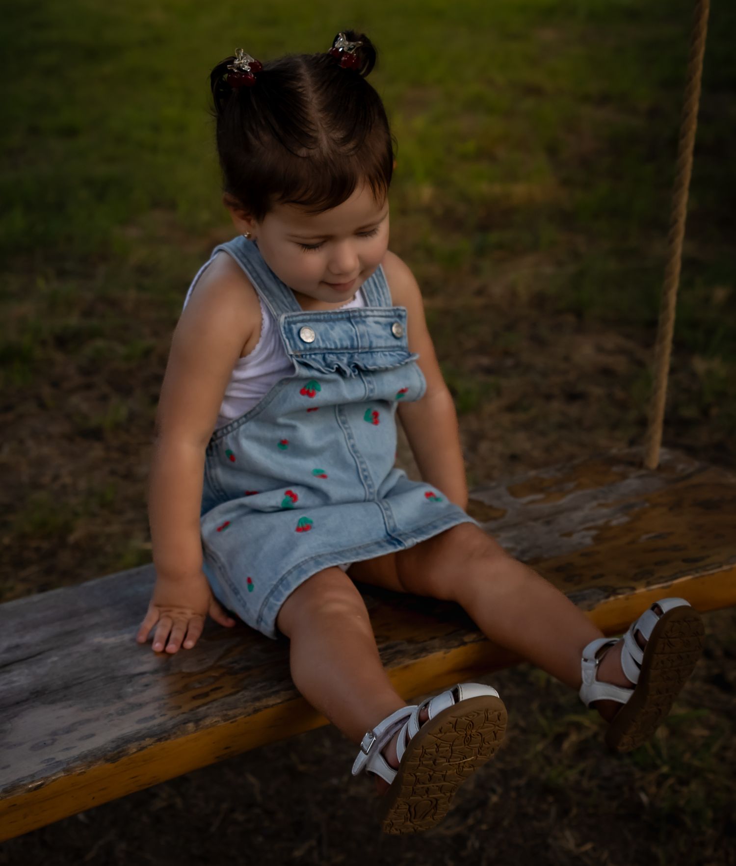 Child in denim overalls sitting on a wooden bench in a natural setting.