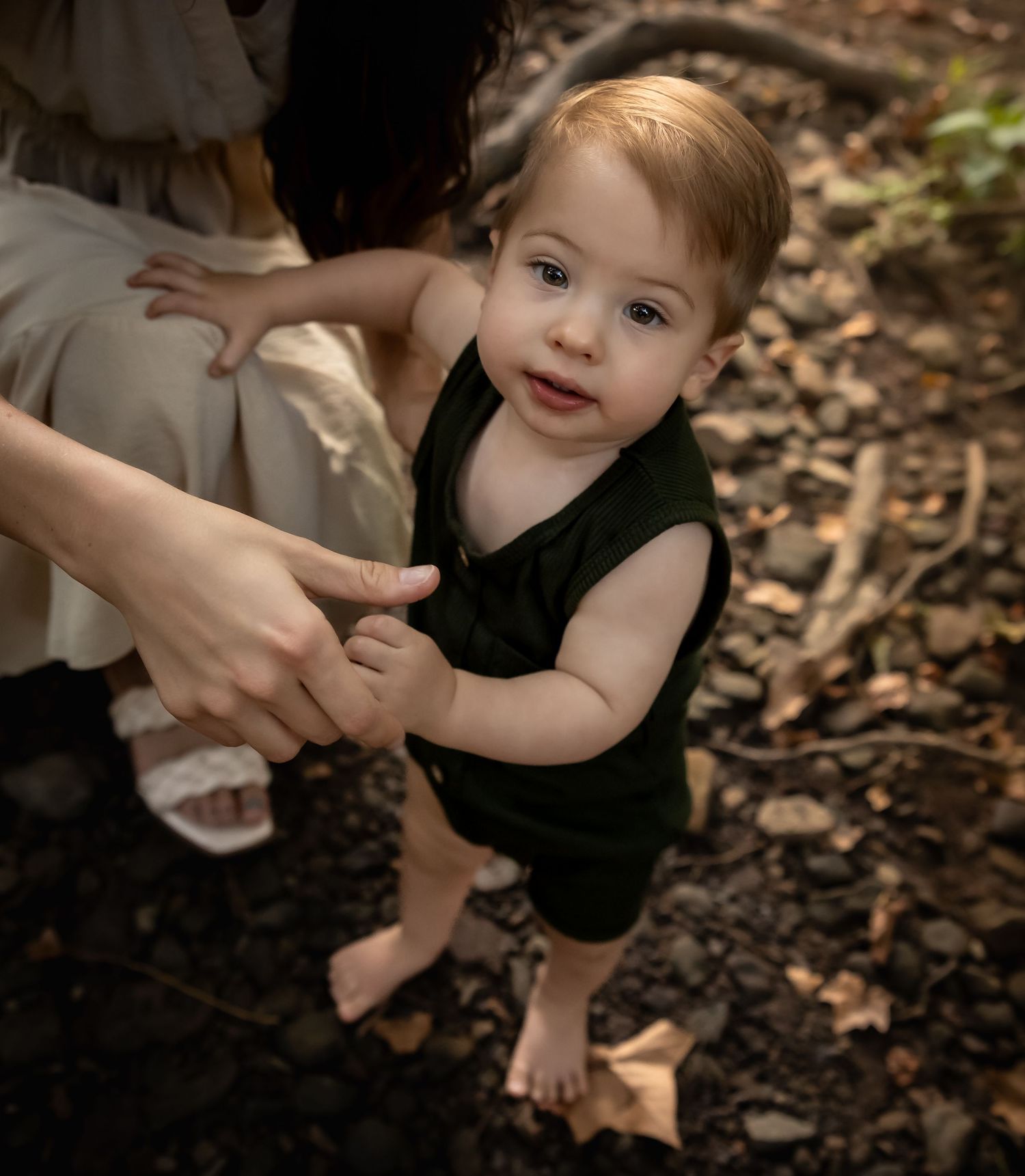 Child in dark green outfit playing on fallen leaves in a forest setting.