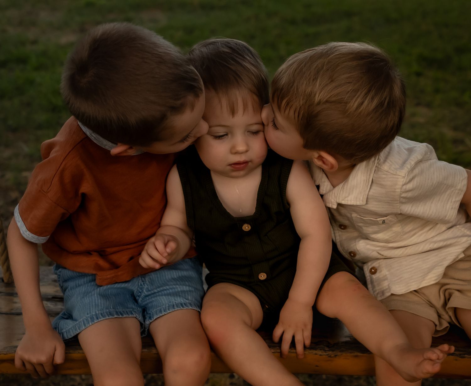 Group sitting together on wooden swing in garden setting during golden hour.