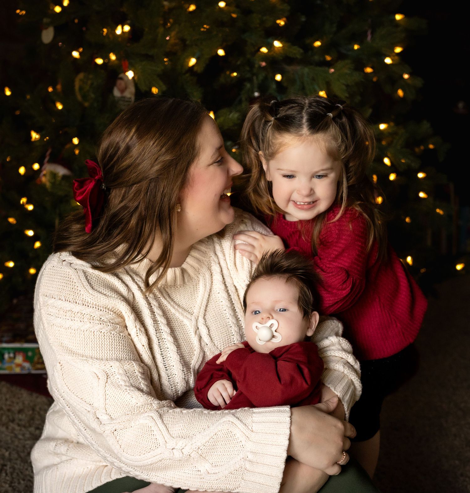 A cozy family holiday portrait in front of a Christmas tree with twinkling lights in the background.