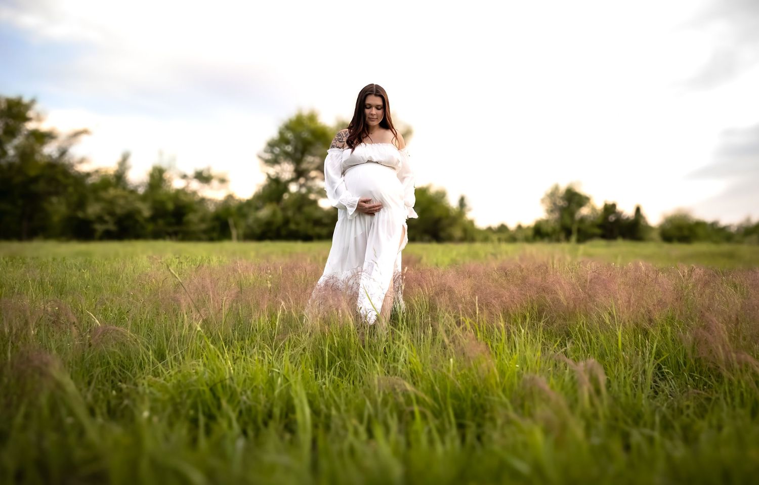 Panoramic view of figure in white dress standing in tall grass during golden hour.