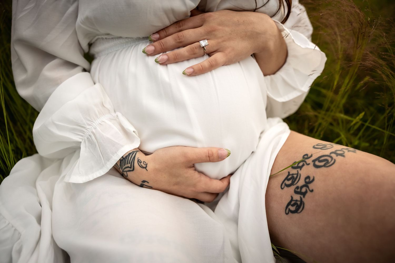Close-up details of hands resting on white fabric with visible tattoo artwork.
