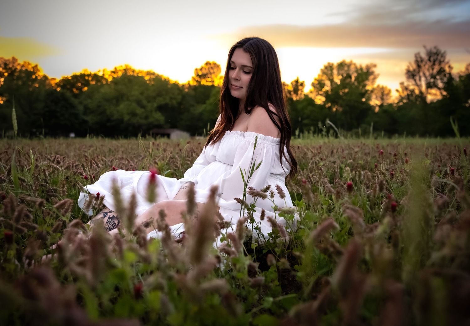 Ethereal sunset maternity photoshoot in a golden field with flowing white dress and natural light.