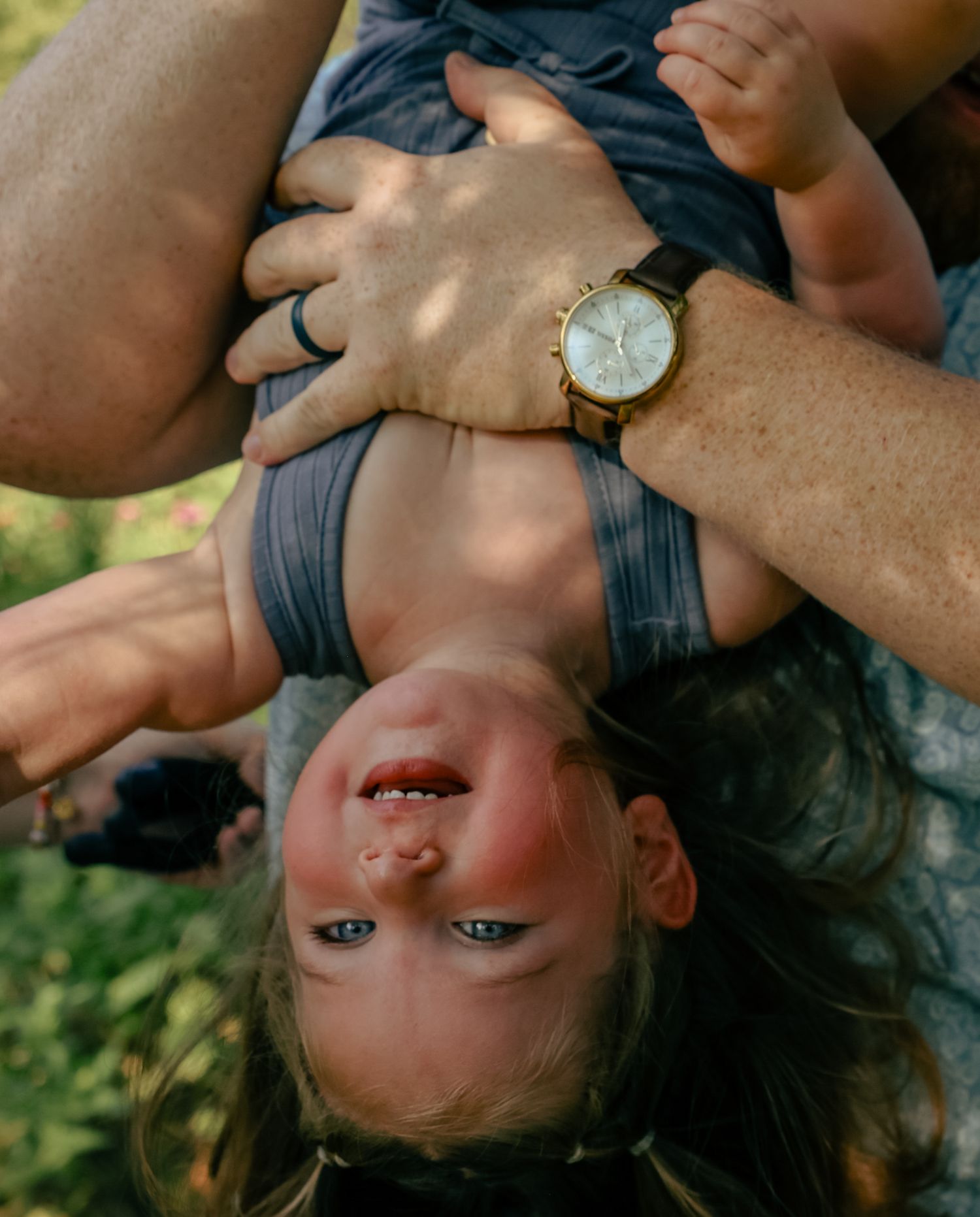 Happy child being playfully held by parent in outdoor setting with natural lighting.