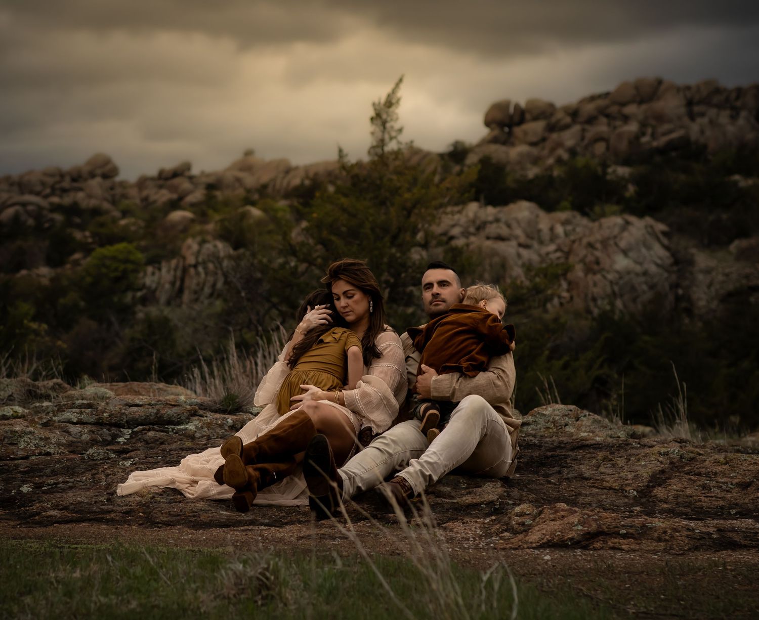 Family relaxing together on rocky outcrop during sunset.