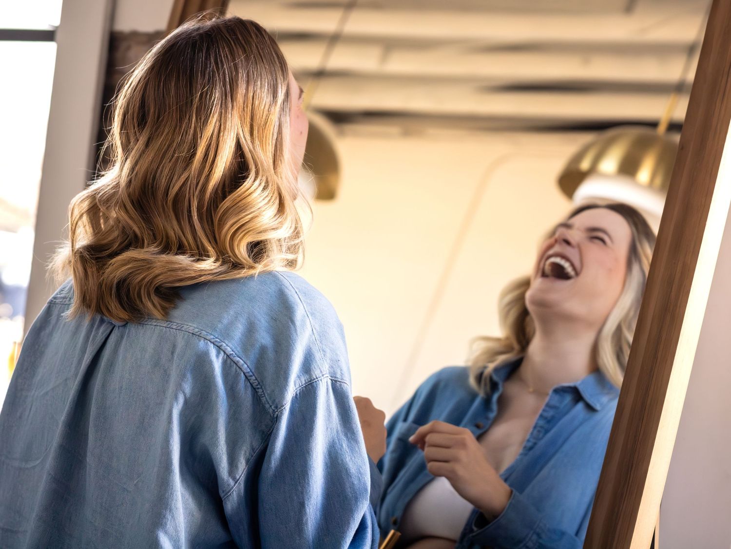 Two people in blue shirts share a tender moment while standing in front of a window.