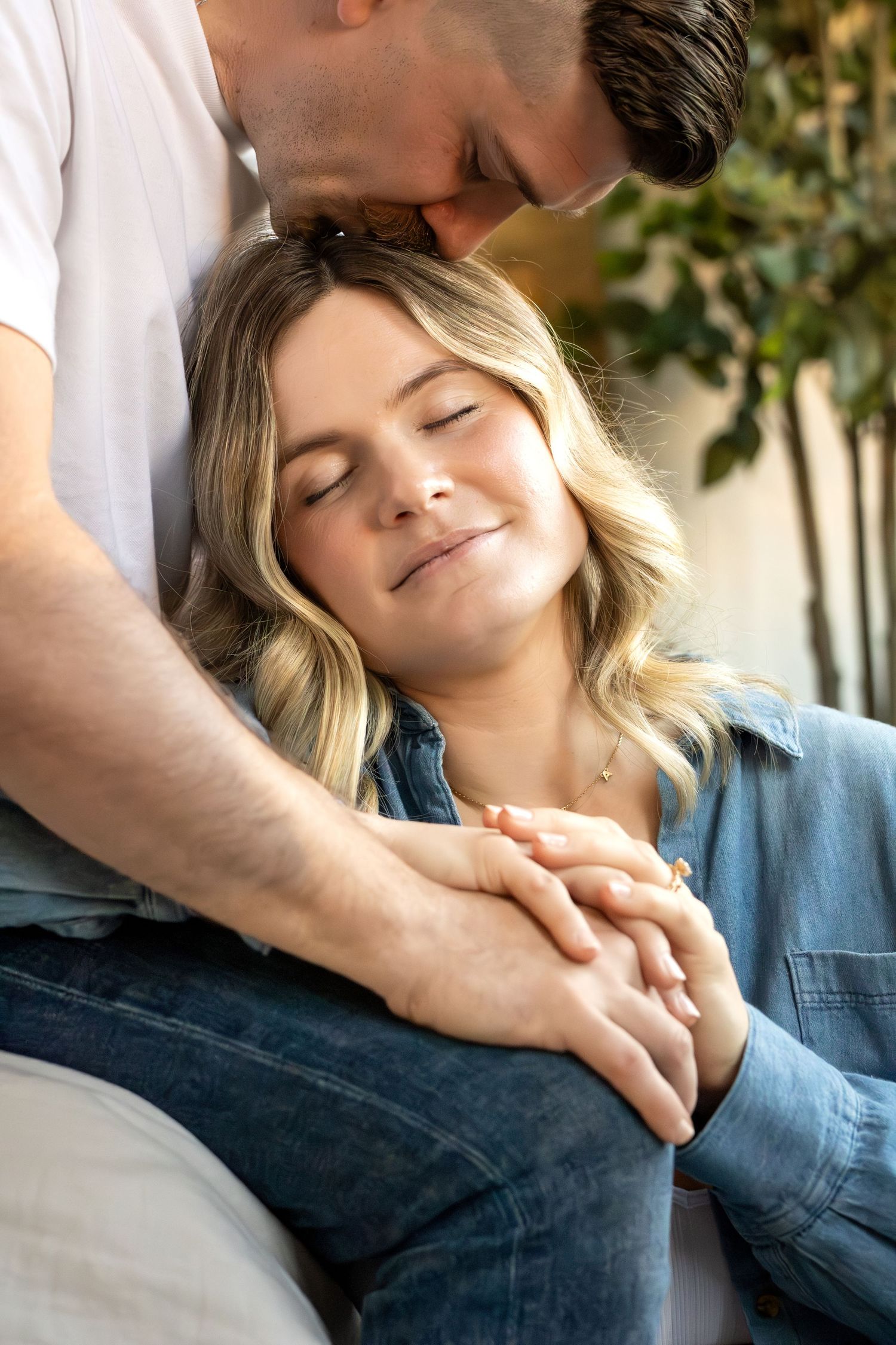 A tender romantic moment between a couple as they embrace with closed eyes in soft natural lighting.