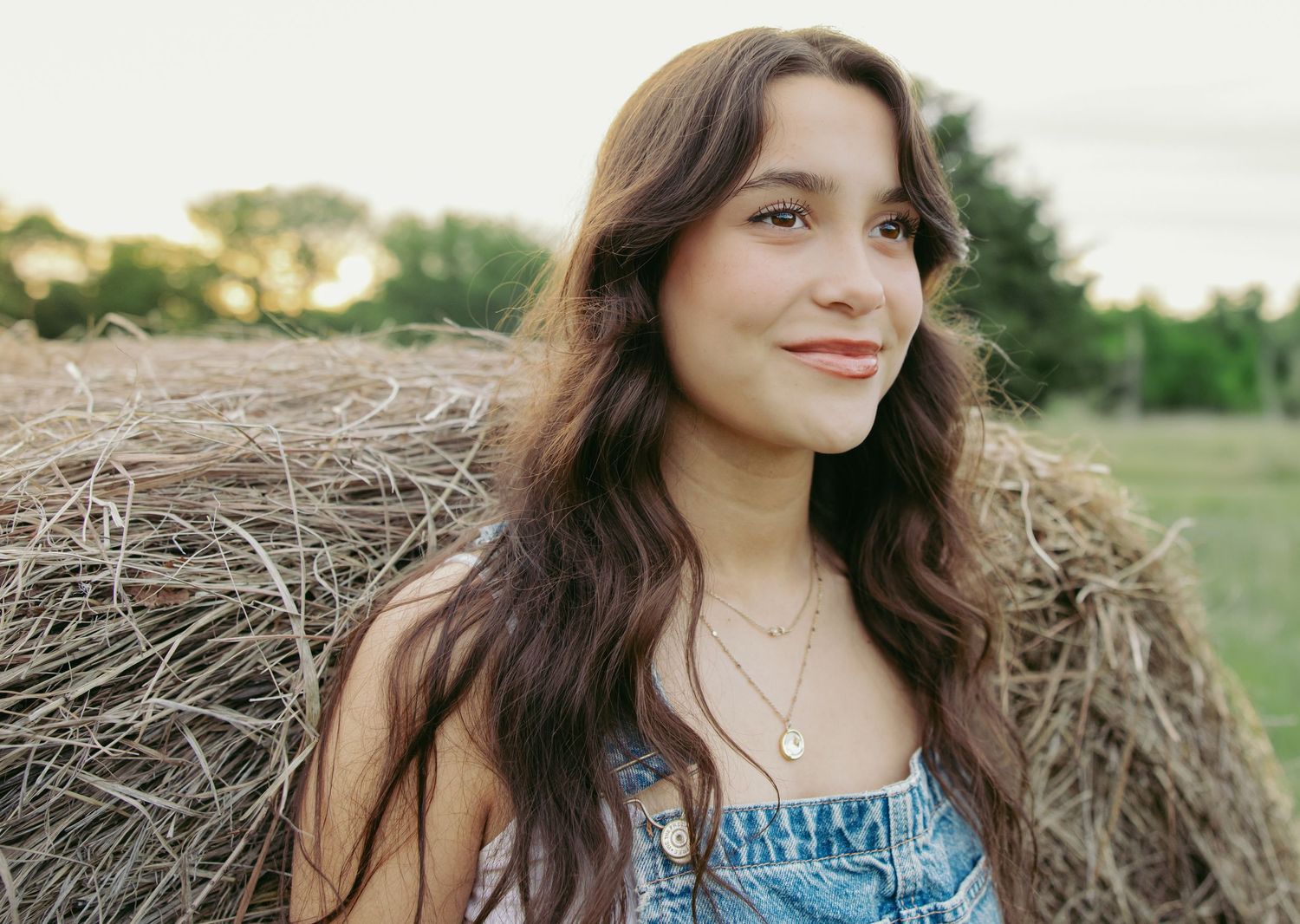 Young woman posing near hay bales in a rustic outdoor setting.