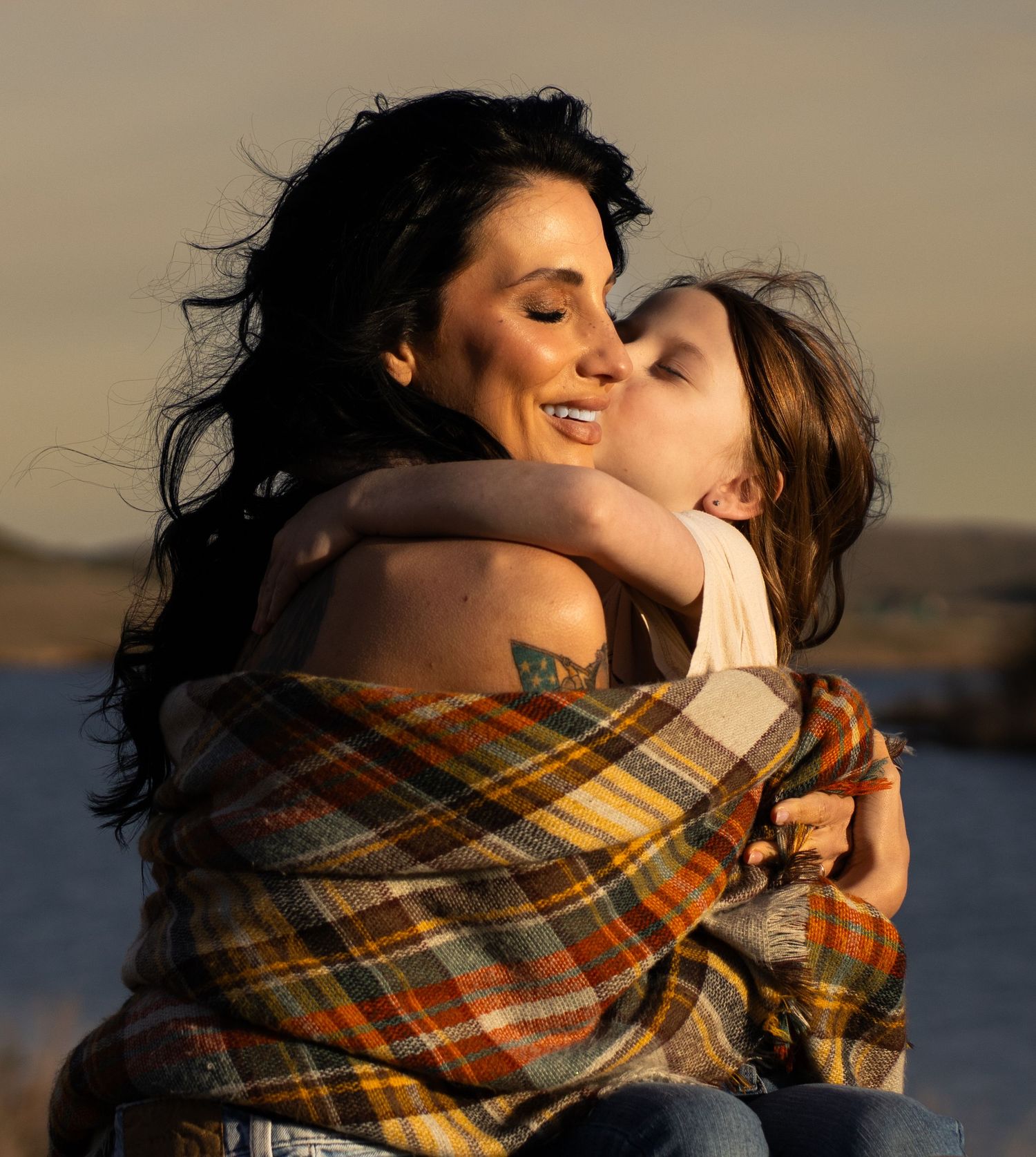Mother and daughter  sharing intimate moment wrapped in plaid blanket at sunset.