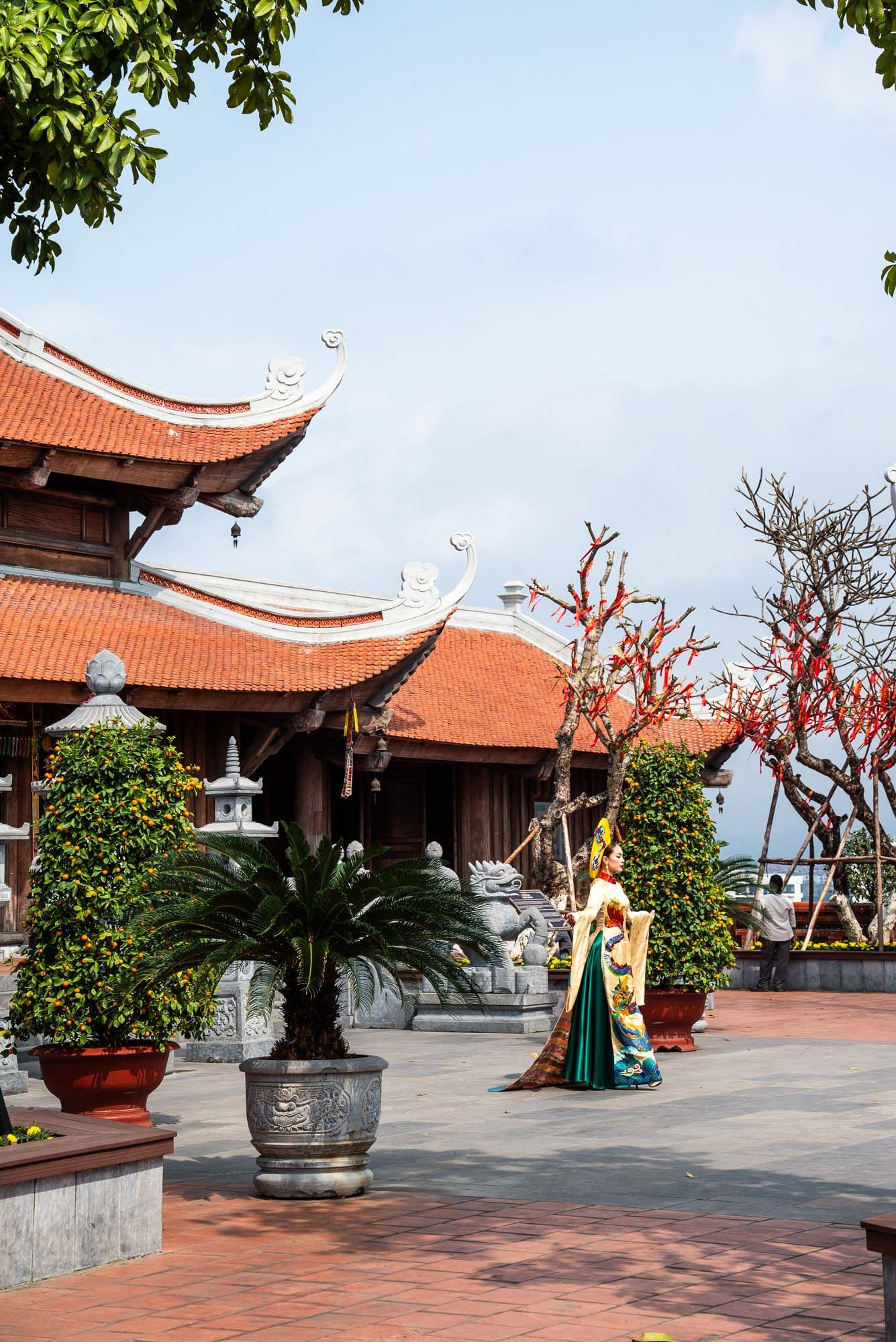 Traditional Vietnamese temple courtyard with orange tiled roofs and potted plants on a sunny day.