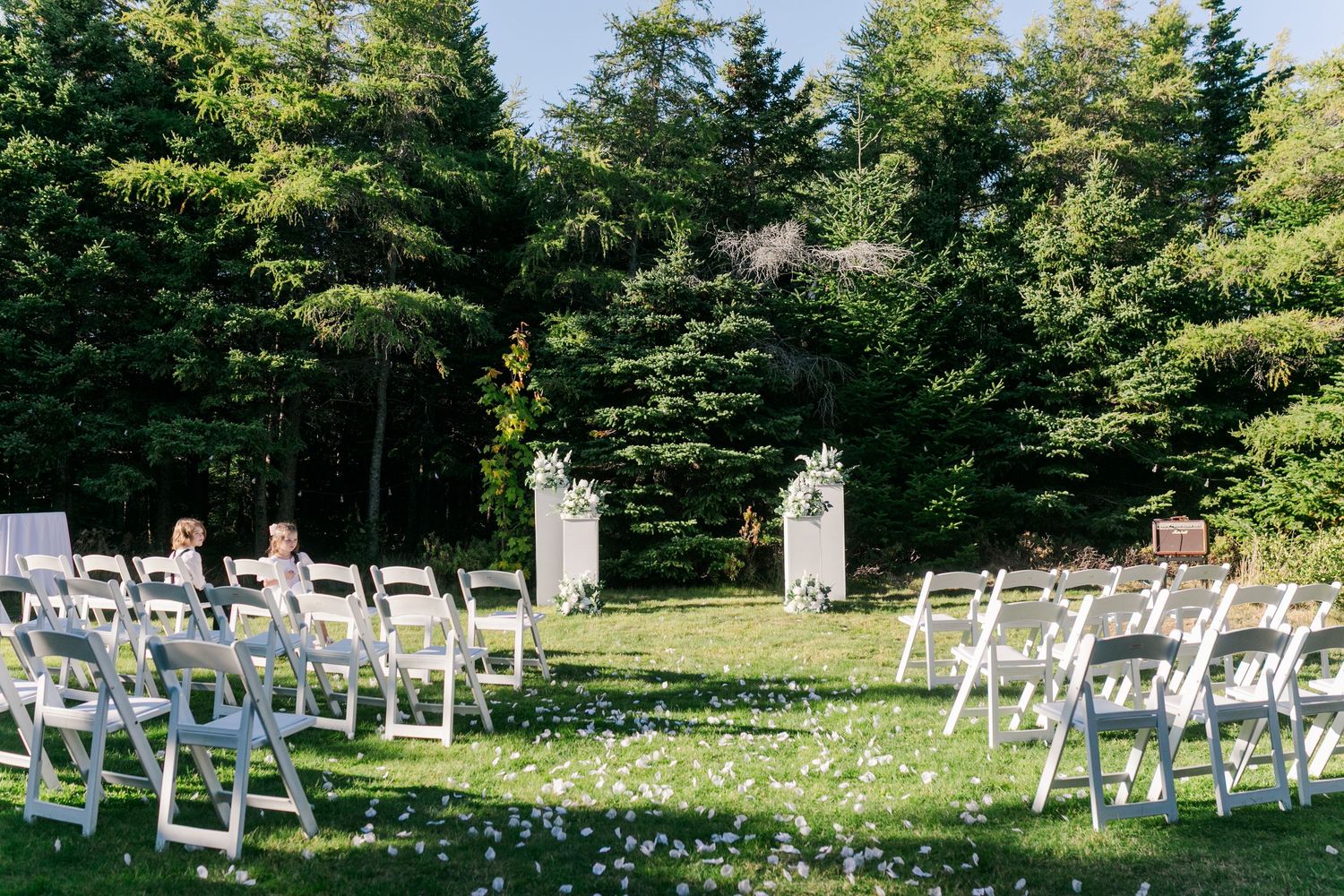 White folding chairs arranged in rows on a lush green lawn for an outdoor wedding ceremony.