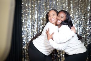 Two people in white tops embracing joyfully against a sparkly silver backdrop.