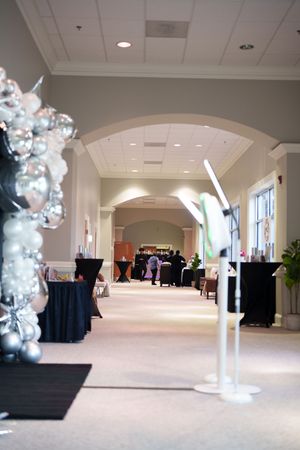 Large white banquet hall with black-draped tables and decorative silver balloon arches preparing for an event.