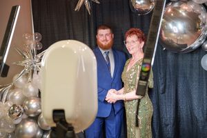Elegant couple posing in front of silver balloon decorations and dark backdrop at formal event.