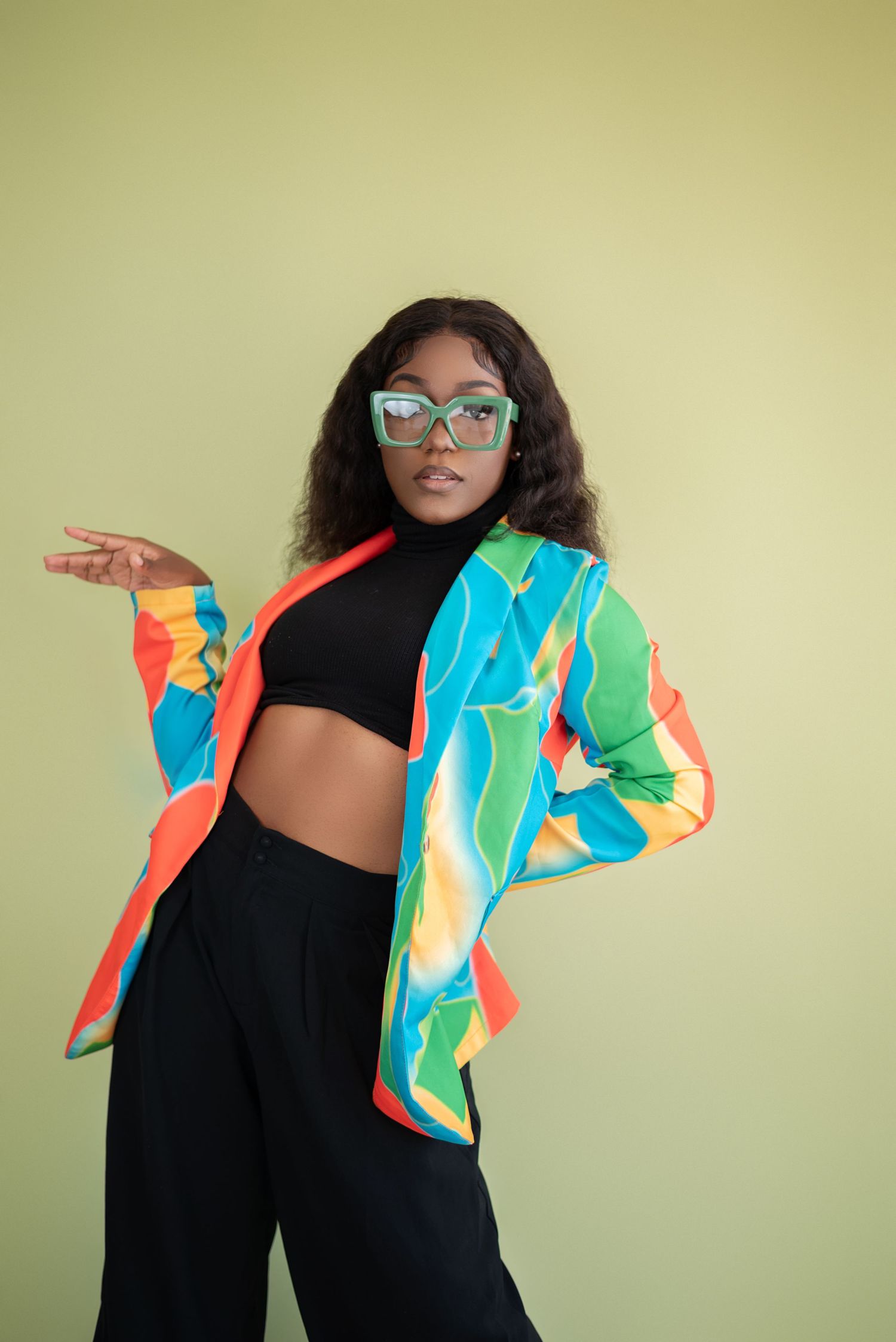 Colorful retro windbreaker jacket in neon blue, green and orange paired with black crop top and pants against olive background.