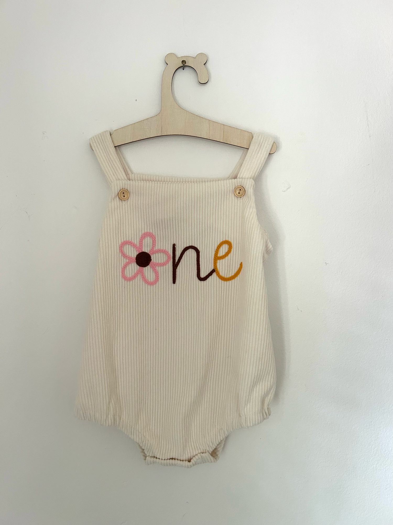 White baby romper with delicate pink embroidered floral design and ruffle details on straps.