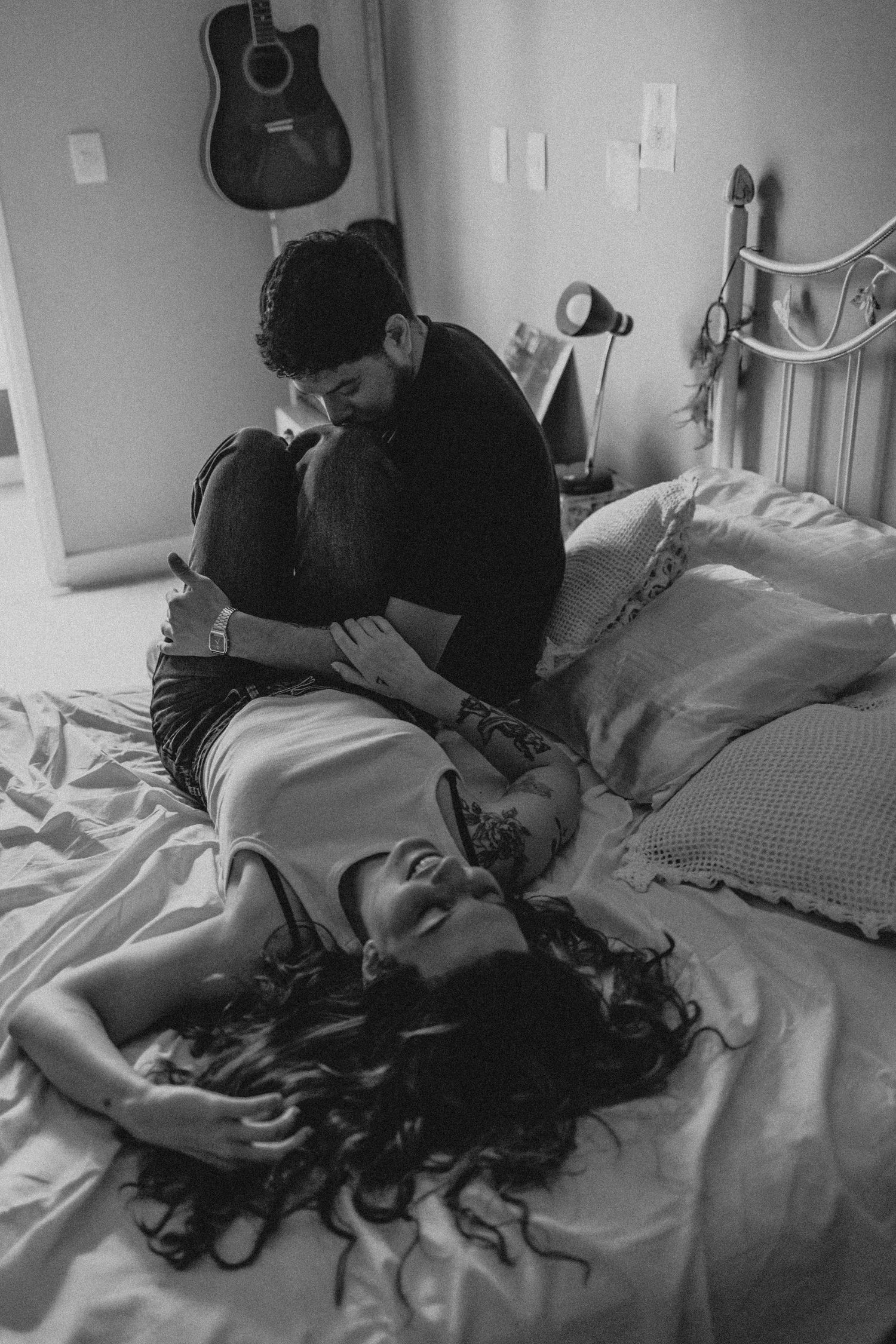 black and white photo of a Couple on the bed, she laid down and he is kissing her knees.