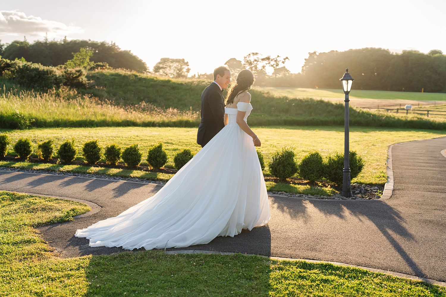 A couple poses for their wedding portrait at sunset on a manicured lawn.