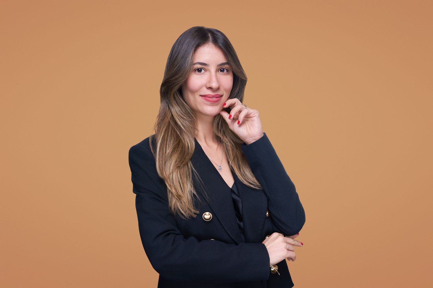 Professional headshot of a person in a black blazer against an orange background.