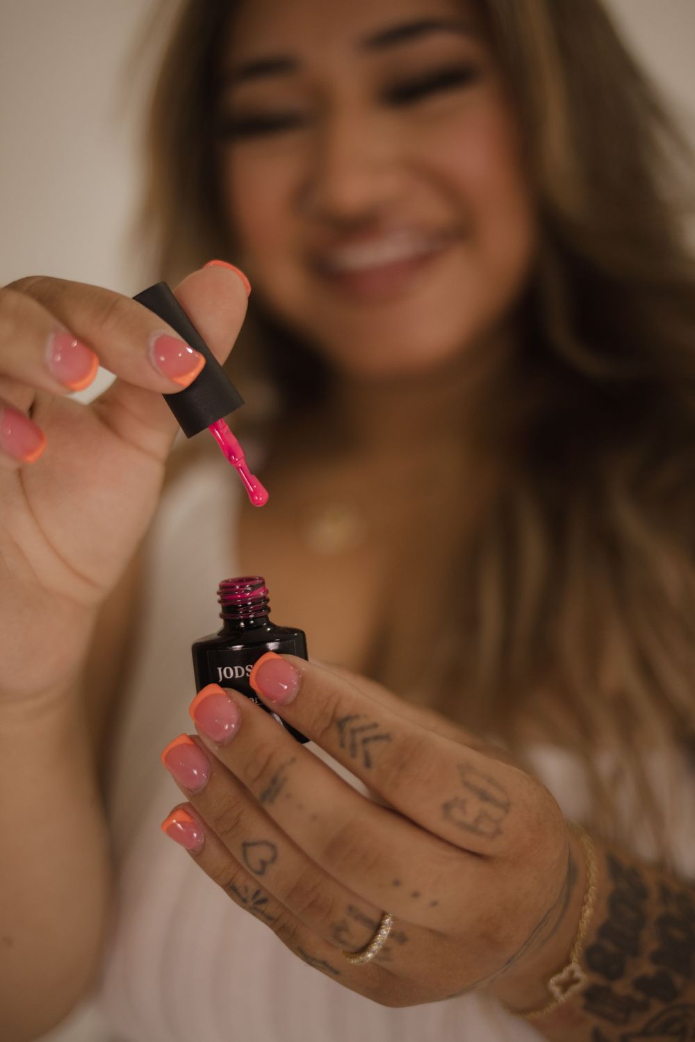Close-up of hands holding pink nail polish bottle with visible tattoos.