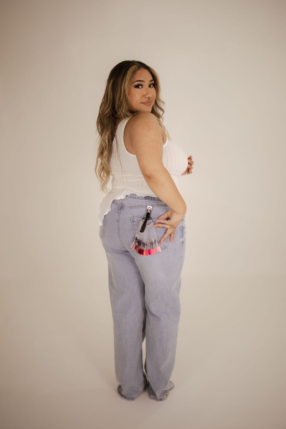 Casual pose wearing light wash denim jeans and white sleeveless top from behind.