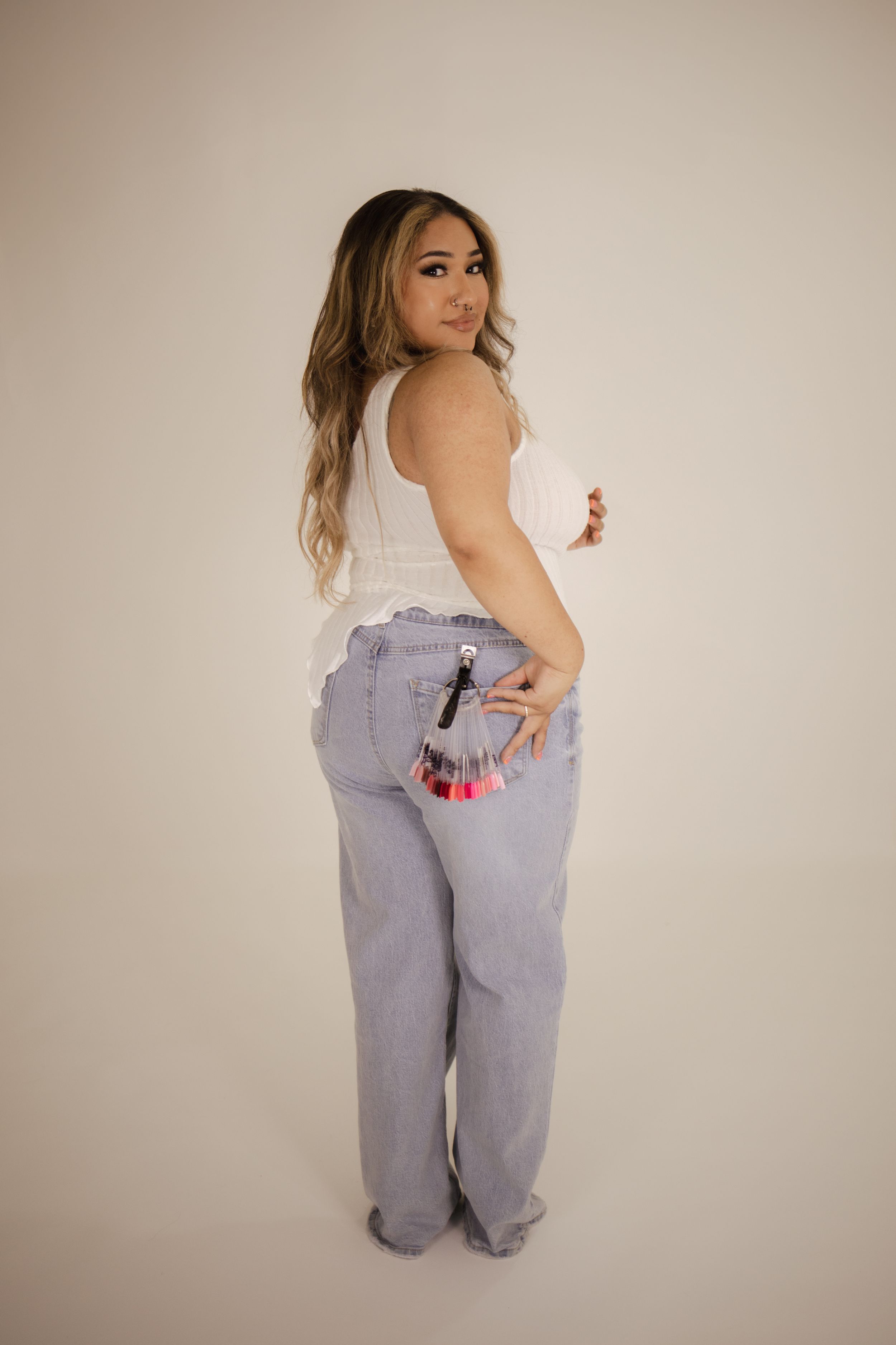 Casual pose wearing light wash denim jeans and white sleeveless top from behind.