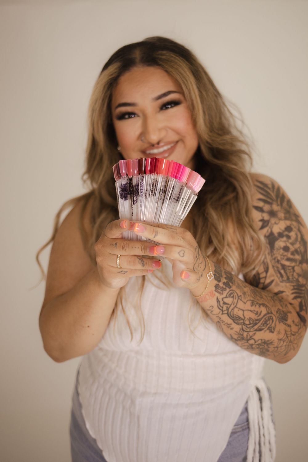 Playful pose holding up nail polish samples while wearing white top.