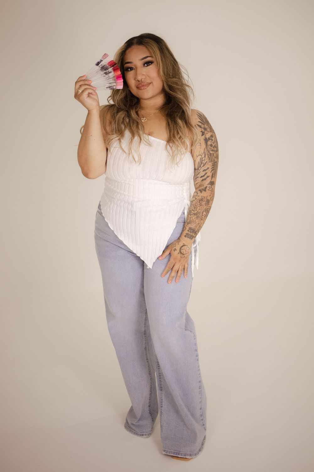 Dynamic pose in white sleeveless top and light wash jeans showing tattoo sleeve.