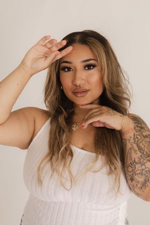 Artistic portrait poses against beige background wearing white summer top.