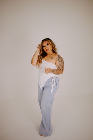 Model wearing a casual white top and light denim dress in a minimalist studio setting.