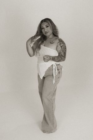 Fashion model in white off-shoulder top and denim dress posing against neutral background.
