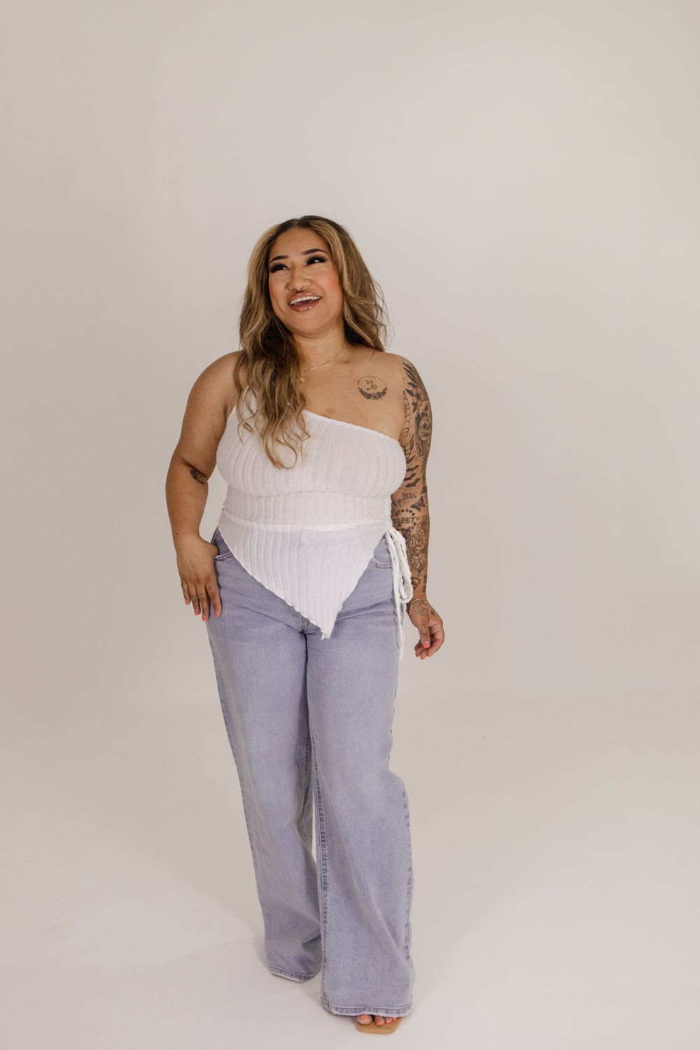 Model showcases casual outfit with white corset top and light denim pants in studio setting.