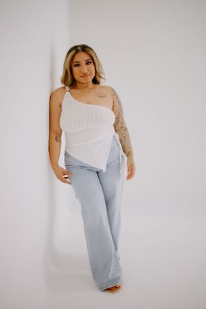 Fashion model posing in white top and light wash denim against white background.