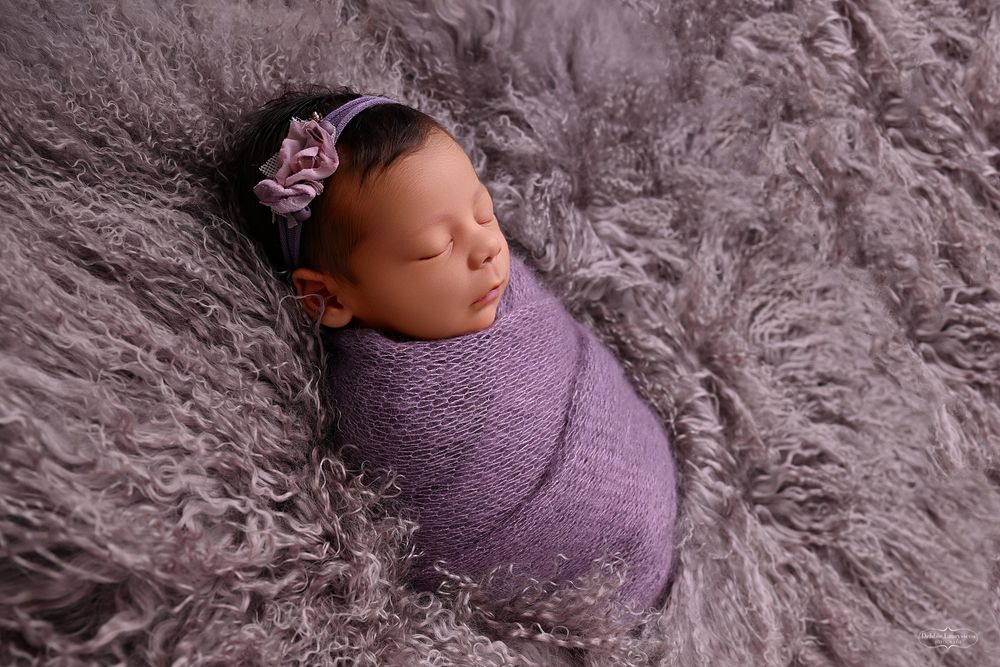 Newborn baby swaddled in purple wrap sleeping on a fur