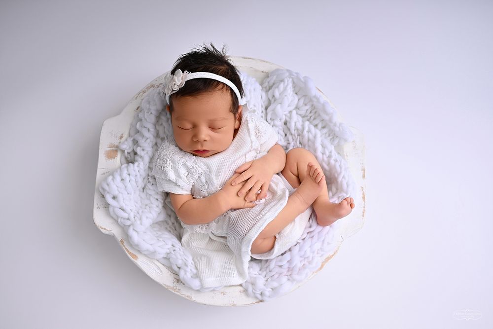 Newborn baby sleeping peacefully on white blanket in bright setting.