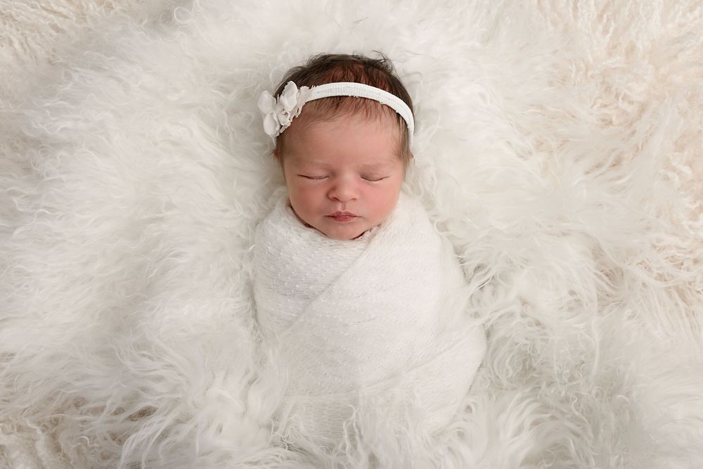 Newborn baby sleeping peacefully on soft white fur blanket.