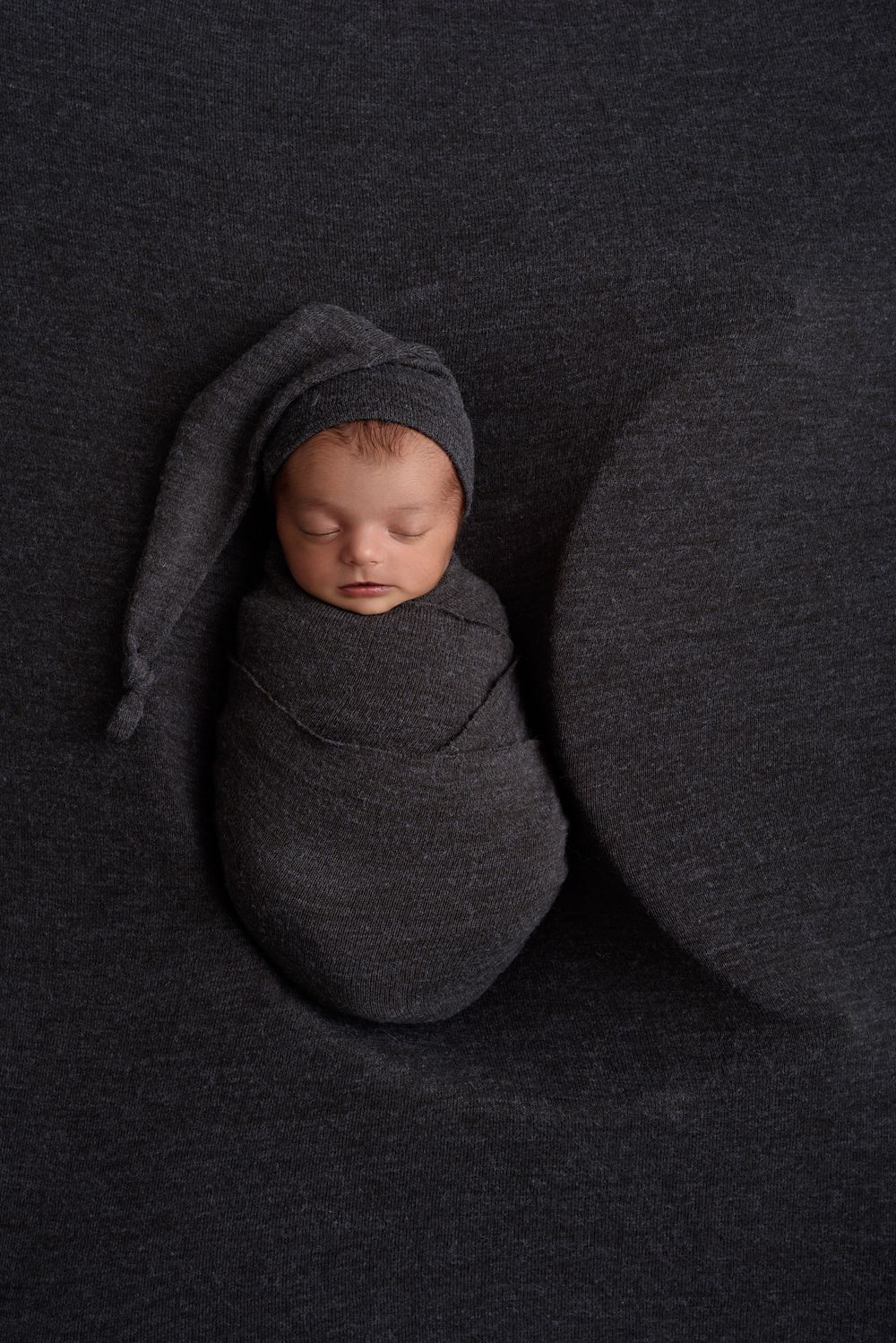 Sleeping newborn swaddled in dark grey wrap in a moon prop.