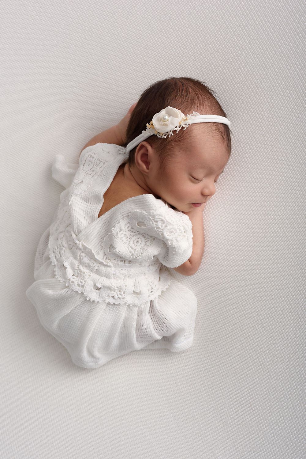 Artistic newborn photography series featuring baby in white lace dress on light background.
