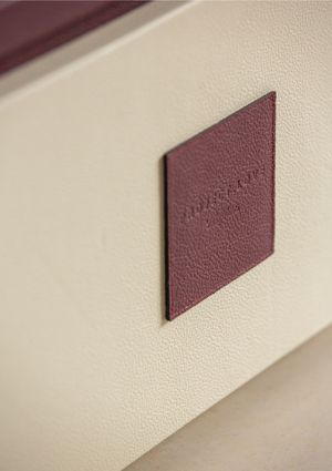 A burgundy leather diamond-shaped emblem mounted on a textured cream-colored wall.