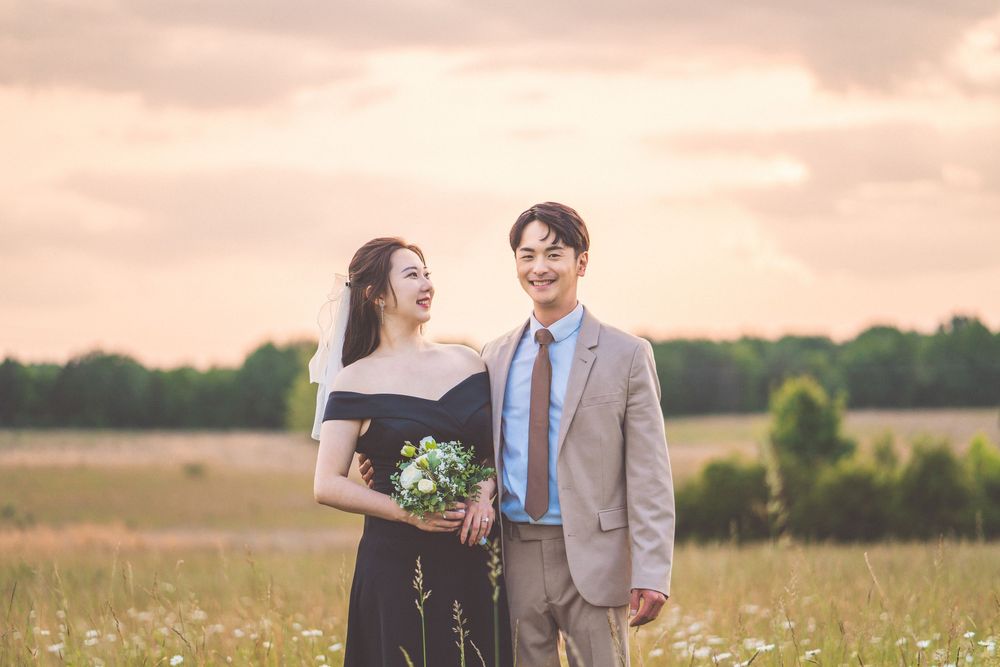 Couple in formal wear sharing a joyful moment in a sunlit meadow with wildflowers.
