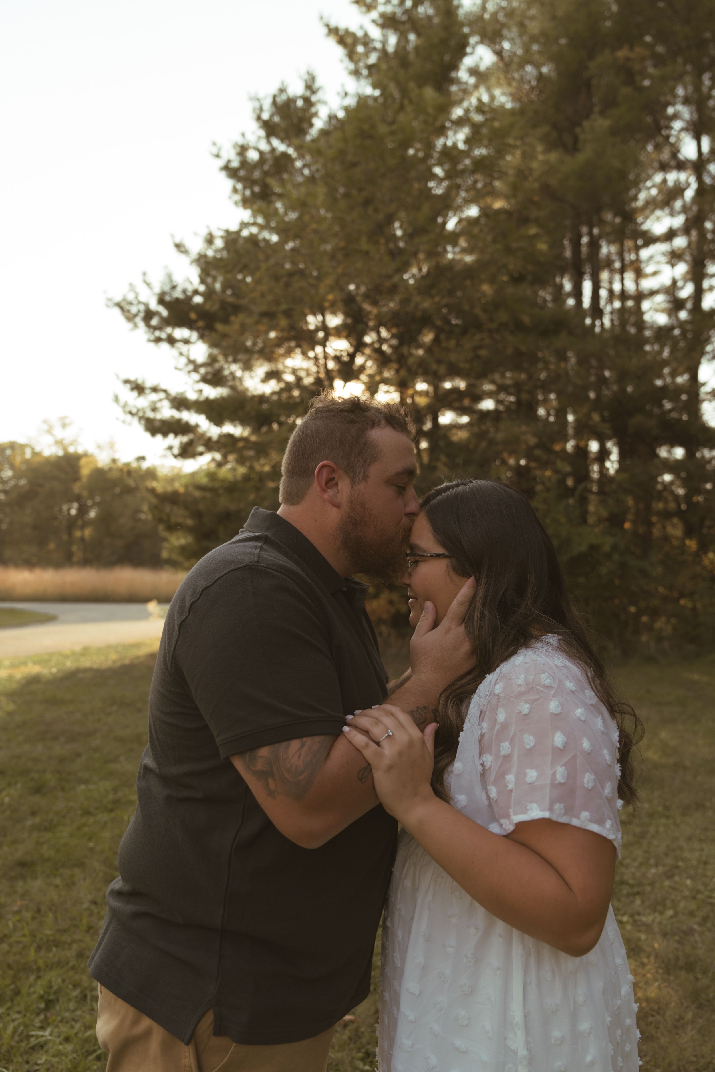 A couple shares tender kisses during a sunset photoshoot among pine trees.