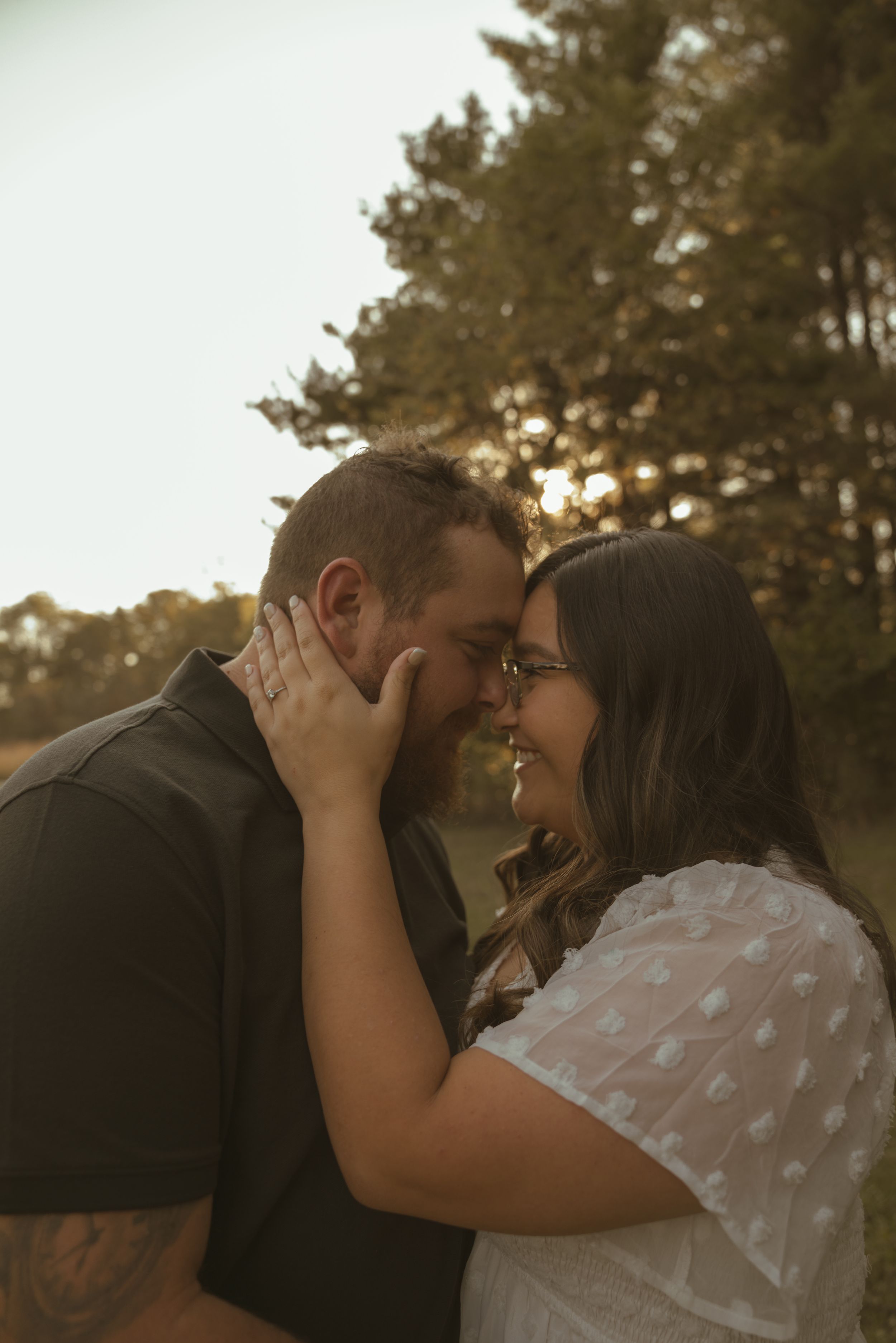 A romantic couple shares an intimate moment at sunset in a natural outdoor setting.