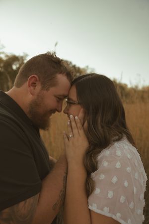 A couple shares a close embrace in a serene outdoor setting with tall grass.