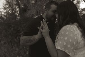 A black and white portrait of a couple embracing in a natural setting.