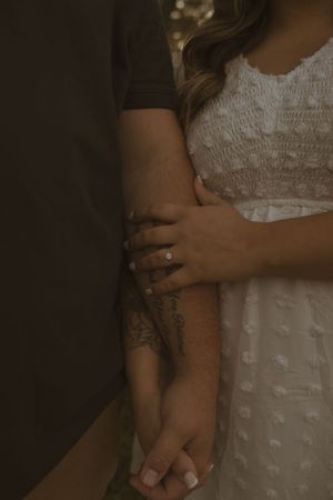 Close-up detail of hands wearing rings against a white lace dress background.