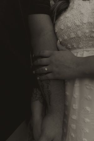 Detail shot of hands resting against a textured white dress in moody lighting.