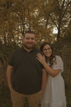 Couple in casual attire standing together against autumn foliage at sunset.